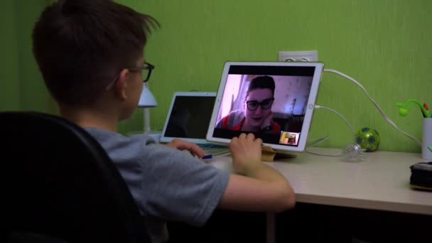 Online-Unterricht. schreibt der Junge eine Notiz vom Tablet-Bildschirm in ein Notizbuch. der Lehrer im kleinen Fenster erklärt das Thema — Stockvideo