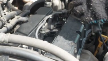 Bir adam arabanın motorundaki yüksek voltajlı kabloları değiştiriyor. Arabanın kaputunun altında çalış. Bujilerin yedeği