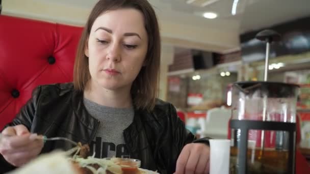 Giovane donna che mangia carne con una forchetta in un ristorante — Video Stock