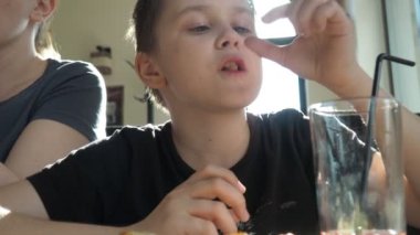 Annesiyle kafede bir genç. Çocuk zevkle yiyor ve içiyor.