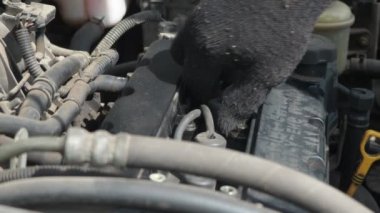 Bir adam arabanın motorundaki yüksek voltajlı kabloları söker. Arabanın kaputunun altında çalış. Bujilerin yedeği
