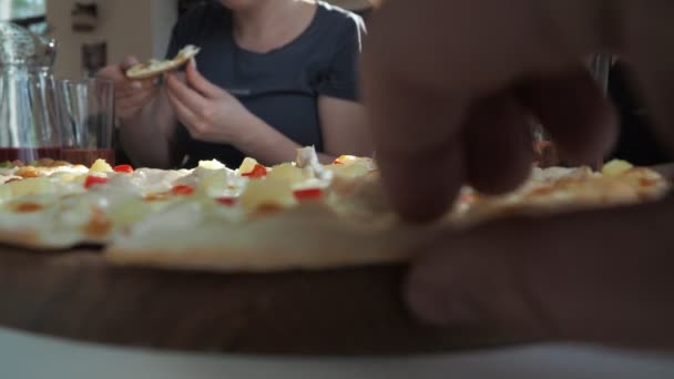 男の手はピザのスライスを取る。背景に子供を持つ女性がチーズを飲んでいます — ストック動画