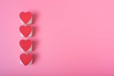 Sol tarafta dikey olarak dört kırmızı kalp, pembe arka plan. Sevgililer gününde aşk ve mutluluk kavramı.