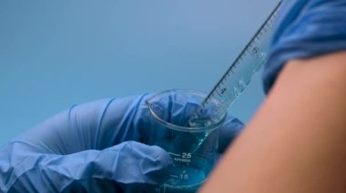 Mavi bir sıvı küçük bir şişeden bir pipetle alınır. Tıbbi araştırma ve geliştirme kavramı.