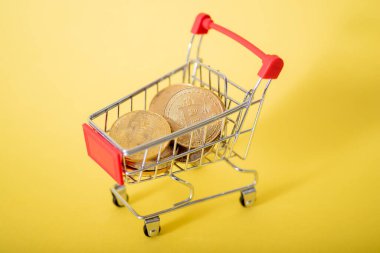 Arabadaki bitcoinler. Kavram: Kripto Para Satın Alma. Dijital Altın. Sarı zemin üzerinde bitcoin olan sepet..