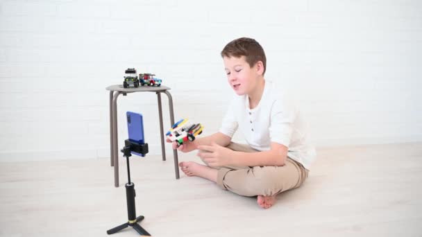 Мальчик-подросток 11 лет блоггер транслирует по телефону о дизайнере и автомобилях с наушниками на свет — стоковое видео