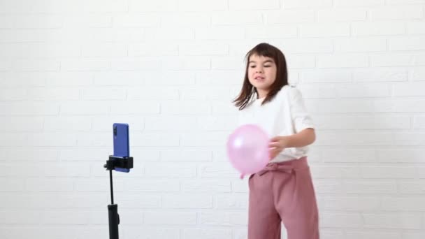 Flicka 8 år gammal bloggare spelar in video på telefonen på en vit bakgrund — Stockvideo