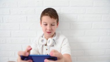 Genç, çocuk 11 yıl duygusal olarak mavi bir telefon çal, sinirlen, gülümse, beyaz bir arka planda yere otur.