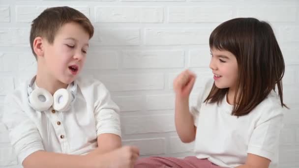 Teenager chlapec 11 let a jeho sestra 8 let jsou vyhozeny na kámen nůžky papír, úsměv, sedět na podlaze na bílém pozadí — Stock video