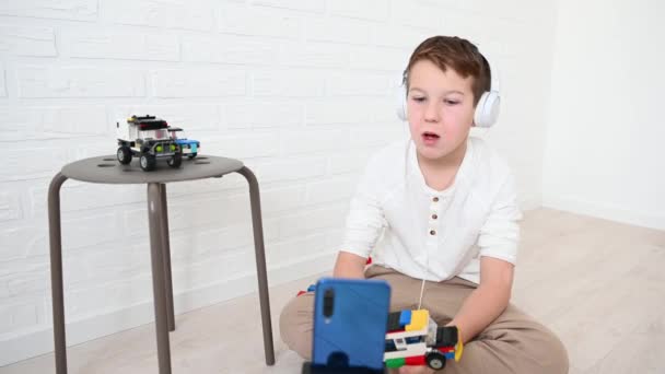 ティーンエイジャーの男の子11歳のブロガーは 光にヘッドフォンで自宅でデザイナーや車についての電話で放送します — ストック動画
