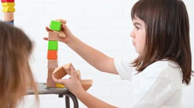 2 mutlu kız kardeş 8 yaşında ve 4 yaşında çocuklar parlak tahta küplerden bir kule inşa ediyorlar oyun oynuyorlar, gülümsüyorlar, beyaz arka planda yere oturuyorlar.