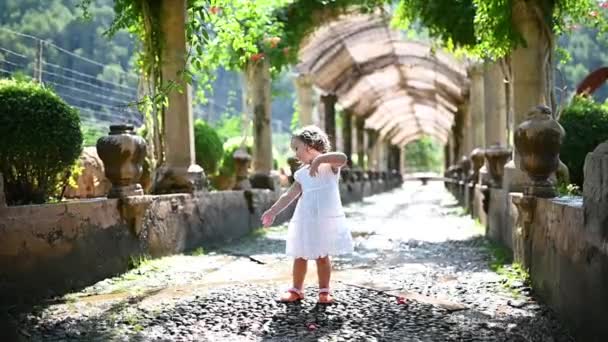 Pequena menina engraçada criança 4 anos de idade em um vestido branco dançando em um belo beco no parque — Vídeo de Stock