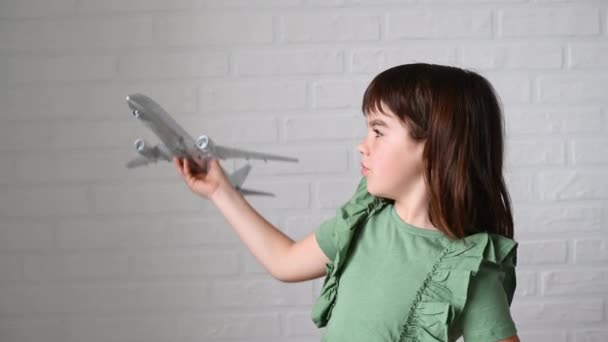Счастливая симпатичная девочка улыбается, играя с самолетом на белом фоне — стоковое видео