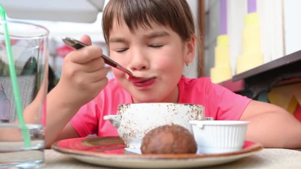 Маленька дівчинка сидить за столом у ресторані, їсть їжу — стокове відео