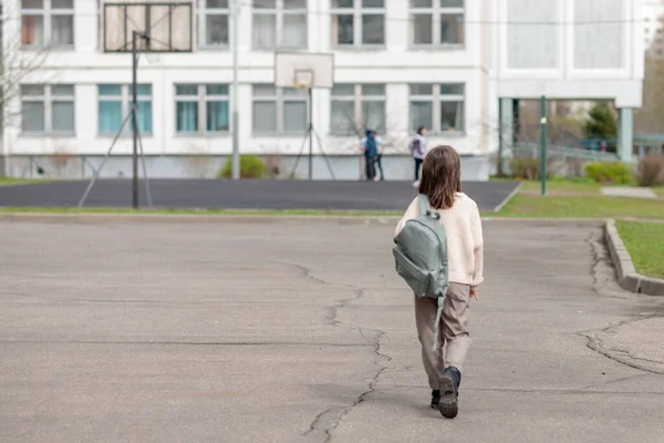 Ragazza felice una studentessa di 8 anni di aspetto europeo con uno zaino sta camminando nel cortile della scuola nel pomeriggio per strada guardando la fotocamera primo piano — Foto Stock