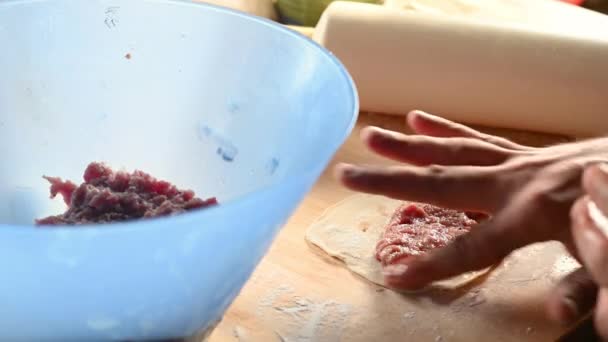 Чоловік на кухні вдома готує паски на столі, розкочує тісто, кладе фарш додому концепцію їжі — стокове відео