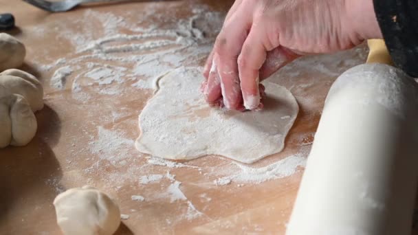 Человек на кухне дома готовит пирожки на столе, выкатывает тесто, кладет фарш на домашнюю еду — стоковое видео