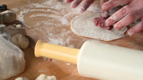 Um homem na cozinha em casa prepara pastéis na mesa, rola a massa, coloca conceito de refeição caseira de carne picada — Vídeo de Stock