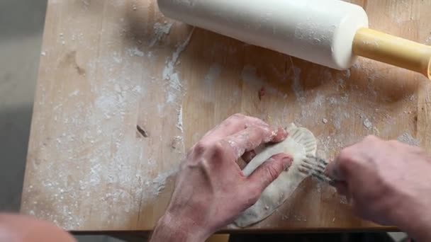 Um homem na cozinha em casa prepara pastéis na mesa, rola a massa, coloca conceito de refeição caseira de carne picada — Vídeo de Stock
