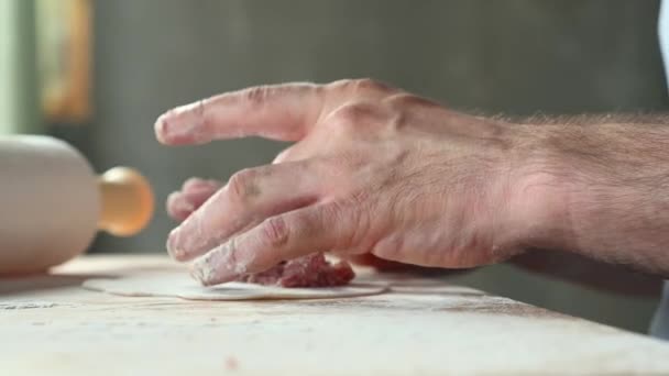 Un homme dans la cuisine à la maison prépare des pâtisseries sur la table, déploie la pâte, met la viande hachée concept de repas à la maison — Video