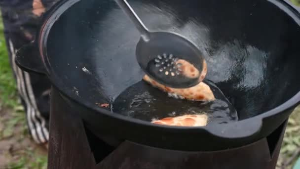 Un homme prépare des pâtés dans un chaudron sur un feu de camp dans la rue dans le pays pendant la journée, il interfère avec une cuillère — Video
