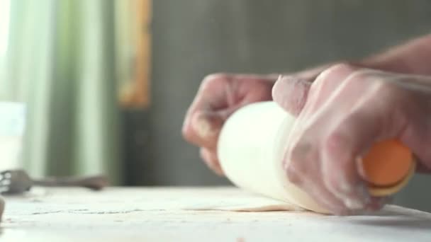 Человек на кухне дома готовит пирожки на столе, выкатывает тесто, кладет фарш на домашнюю еду — стоковое видео