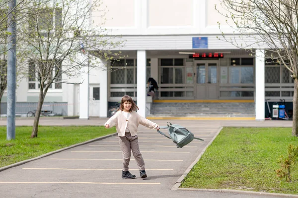 Ragazza felice una studentessa di 8 anni di aspetto europeo con uno zaino sta camminando nel cortile della scuola nel pomeriggio per strada guardando la fotocamera primo piano — Foto Stock