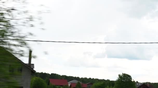 Blick aus dem Autofenster im Dorf auf die grünen Bäume Säulen des Hauses tagsüber bei Regen und grauem Himmel — Stockvideo