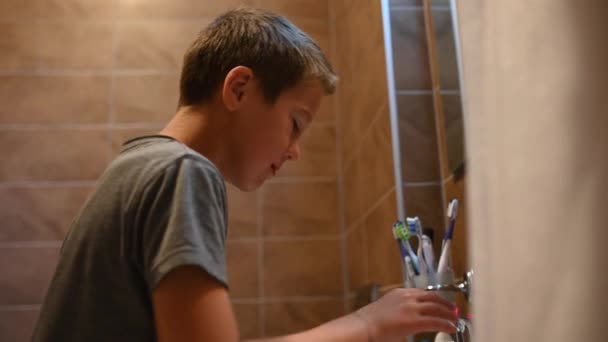 Een jongen van 11 jaar oud schooljongen poetst zijn tanden en wast zich met water in de badkamer — Stockvideo