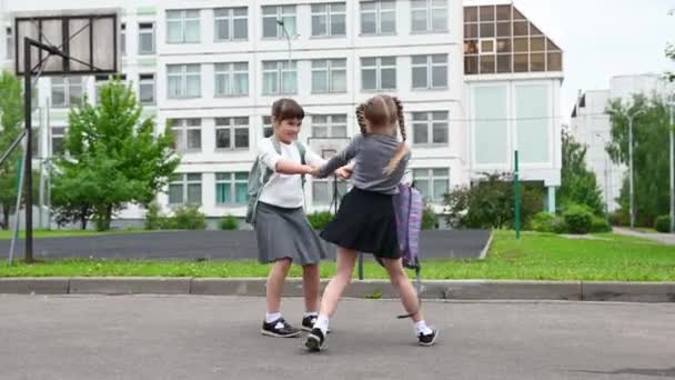 Dos niñas felices lindas colegialas con mochilas están jugando cerca de la escuela — Vídeo de stock