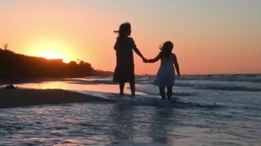 Yazın gün batımında deniz kıyısında uzun saçlı küçük bir kız çocuğu kumsalda koşuyor.