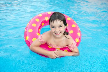 Parlak bir çemberdeki tatlı, gülümseyen kız yazın mavi bir havuzda yüzer.