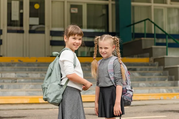 Δύο χαριτωμένα ευτυχισμένα κορίτσια μαθήτριες με σακίδια παίζουν κοντά στο σχολείο — Φωτογραφία Αρχείου