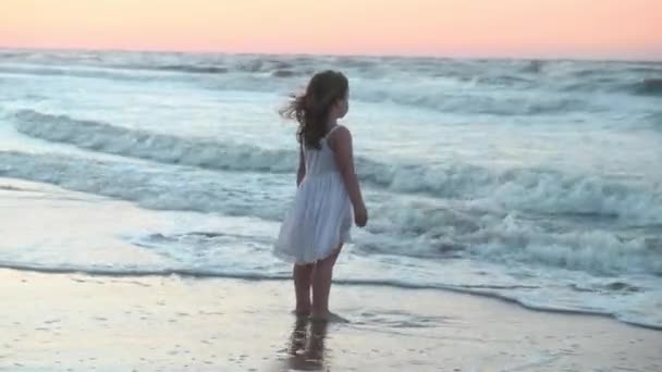 Little girl child in a long sundress with long hair runs along the beach along the sea at sunset in summer — Stock Video