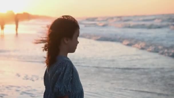 Menina criança em um longo vestido de verão com cabelos longos corre ao longo da praia ao longo do mar ao pôr do sol — Vídeo de Stock