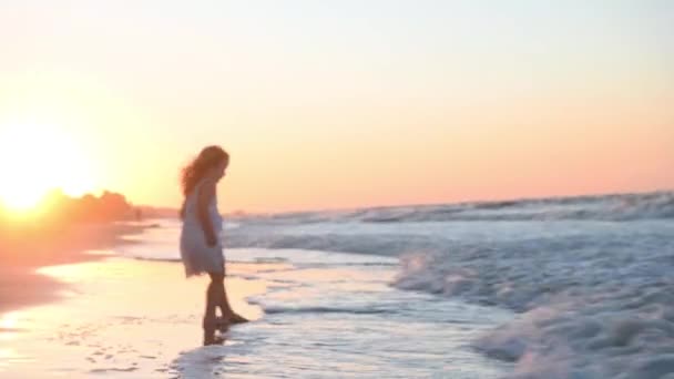 Fetiță copil într-o rochie lungă de soare cu păr lung aleargă de-a lungul plajei de-a lungul mării la apusul soarelui în timpul verii — Videoclip de stoc