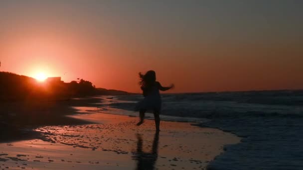 Petite fille enfant dans une longue robe de soleil avec de longs cheveux court le long de la plage le long de la mer au coucher du soleil en été — Video