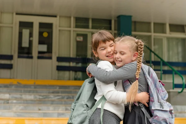Dos niñas felices lindas colegialas con mochilas están jugando cerca de la escuela — Foto de Stock