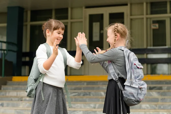 Dos niñas felices lindas colegialas con mochilas están jugando cerca de la escuela —  Fotos de Stock