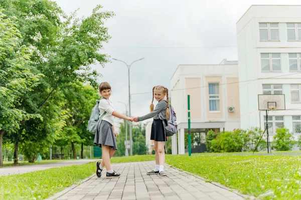 Zwei süße, glückliche Schulmädchen mit Rucksäcken spielen in der Nähe der Schule — Stockfoto