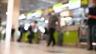 Bulanık görüntülü, bavullu, tıbbi maskeli insanlar havaalanı seyahat konseptinde kayıt gişelerinin önünden geçiyorlar.