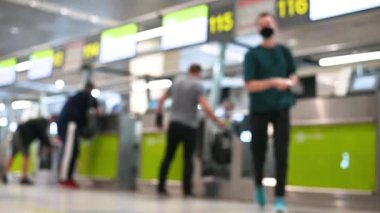 Bulanık görüntülü, bavullu, tıbbi maskeli insanlar havaalanı seyahat konseptinde kayıt gişelerinin önünden geçiyorlar.