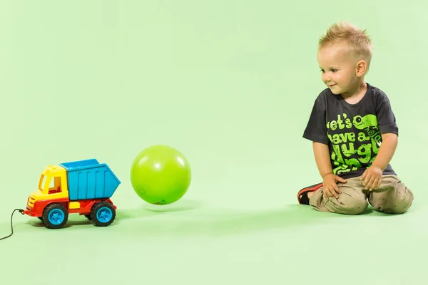 Blond boy playing with colorful car toy green background — Stock Photo, Image