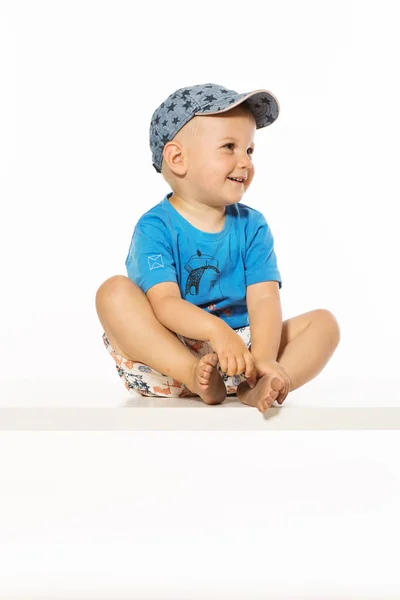 Blond lachende jongen zittend op de tafel dragen Baseballpet — Stockfoto
