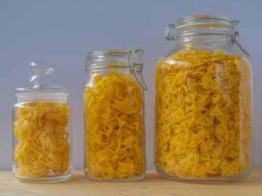 Farklı boyutlarda makarnalarla dolu cam kavanozlar ahşap masada, kapat.