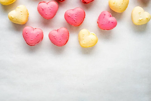 yellow and pink pastel colored heart shaped french macarons  on top on white textured background, close up, copy space