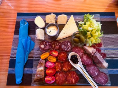 Cam tabakta şarküteri çeşitleri. Geleneksel Katalonya usulü salam, siyah zeytin reçeli ve peyniri restorandaki masa düzeninde, yüksek açı manzaralı.