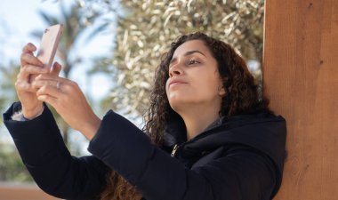 Genç kız akıllı bir telefona bakıyor ve parkta sevişiyor.