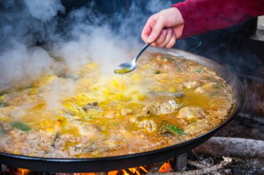 Geleneksel Valensiyalı paella pişirme süreci: İspanya 'da tuz seviyesindeki Akdeniz mutfağını kontrol etmek için çorba tatmak.