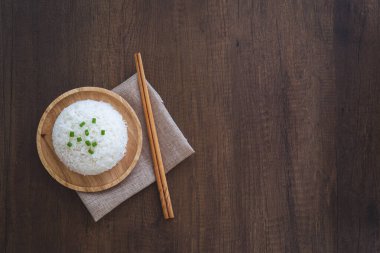 Ahşap bir tabakta, üzerinde yeşil soğan dilimleri, yemek çubukları ve ahşap bir masada servis altlığı olan beyaz pirinç pişirdim. Tayland Jasmine pirinci..
